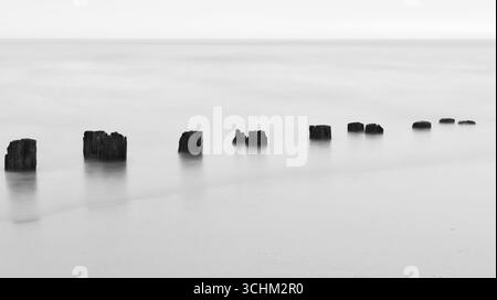 Ruhige Küstenszene mit Holzpfosten und glatter Wasseroberfläche Stockfoto