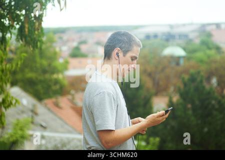 Mann, der mit einem Smartphone telefoniert oder eine Videokonferenz abnimmt und von außen aus arbeitet. Symbolisiert flexibles Arbeiten – von überall aus. Digitaler Nomade Stockfoto