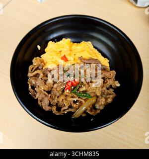 Köstliches Rührfleisch mit Rührei serviert auf Reis in schwarzer Schüssel, asiatisches Komfortgericht mit herzhaftem Geschmack Stockfoto