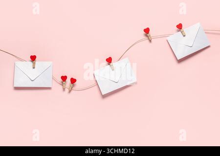 Umschläge hängen an einem Seil vor farbigem Hintergrund. Valentinstag-Feier Stockfoto