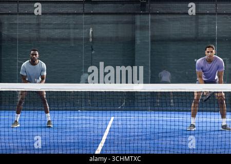 Verschiedene männliche Tennismannschaftskameraden warten auf dem blauen Platz hinter Netzhaltern Stockfoto