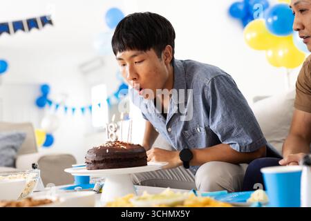 Asiatischer Teenager, der Kerzen auf Geburtstagskuchen zu Hause ausbläst Stockfoto