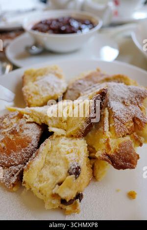 Frisch zubereiteter Kaiserschmarrn, ein traditionelles österreichisches Pfannkuchendessert, serviert auf einem weißen Teller und großzügig mit Puderzucker bestäubt Stockfoto