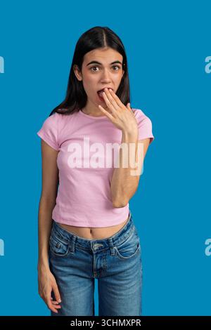 Studio-Porträt einer überraschten jungen Frau, die ihren Mund mit der Hand bedeckt und Schock und Unglauben ausdrückt Stockfoto