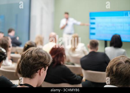 Gruppe von Personen, die an einer Präsentation teilnehmen, in der der Sprecher mithilfe von visuellen Hilfsmitteln Konzepte erklärt Stockfoto