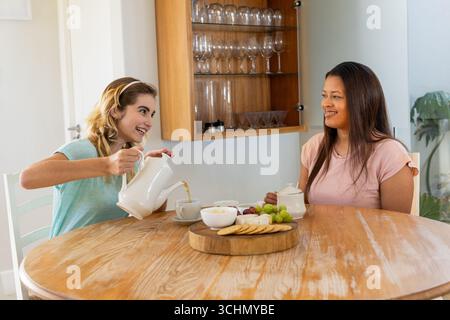 Verschiedene Freundinnen genießen zu Hause Tee und Snacks, lächeln und plaudern fröhlich Stockfoto