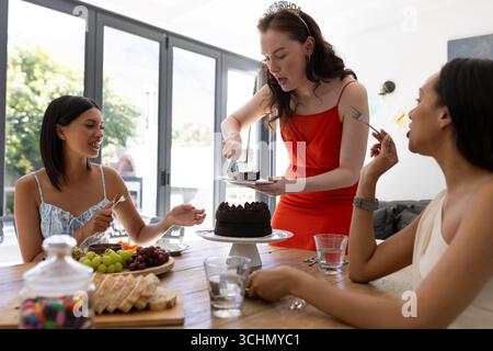 Schokoladenkuchen schneiden, eine junge Frau mit langen braunen Haaren feiert mit Freunden Stockfoto