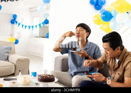 Vater und Sohn genießen Kuchen und Snacks zu Hause während der festlichen Feier mit Ballons Stockfoto