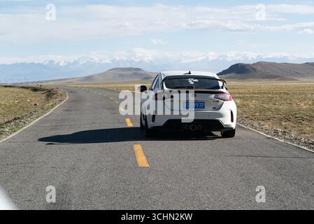 Eine weiße heiße Luke fährt entlang eines geschwungenen Hochplateaus in Richtung eines weit entfernten, weitläufigen, schneebedeckten Gebirges. Stockfoto