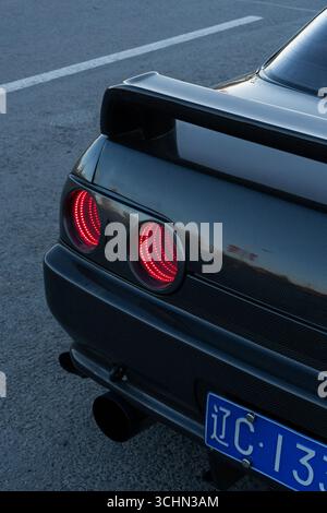 Nahaufnahme des Hecks eines Sportwagens aus Kohlefaser mit leuchtend roten Infinity-Spiegeln und einem schlanken Spoiler. Stockfoto