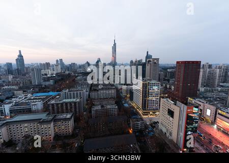 Blick aus der Vogelperspektive auf eine dichte Skyline der Stadt in der Abenddämmerung mit einem hochaufragenden Wolkenkratzer, modernen Gebäuden und leuchtenden Straßen. Stockfoto