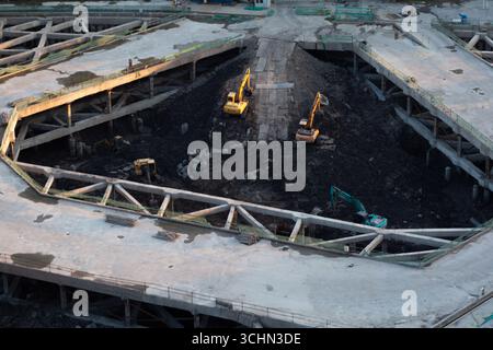 Luftaufnahme einer Tiefbaugrube mit gelben Baggern, die Schmutz unter schweren Betonträgern bewegen. Stockfoto