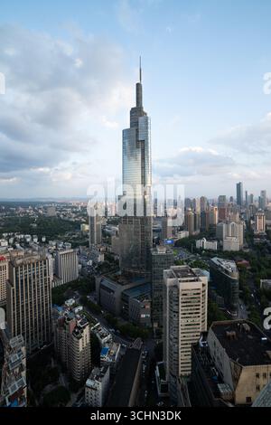 Aus der Vogelperspektive auf einen hohen Glashochhaus mit einem Turm, der eine dichte moderne Skyline unter einem teilweise bewölkten Himmel dominiert. Stockfoto
