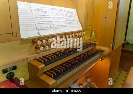 Antike Orgeltastatur und Bedienelemente in einer lutherischen Kirche. Notenblätter mit Notizen liegen auf dem Ständer. Stockfoto