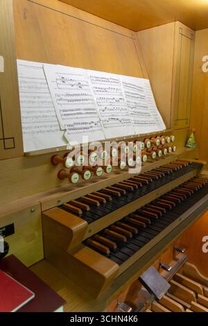 Antike Orgeltastatur und Bedienelemente in einer lutherischen Kirche. Notenblätter mit Notizen liegen auf dem Ständer. Stockfoto