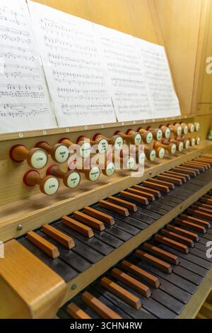 Antike Orgeltastatur und Bedienelemente in einer lutherischen Kirche. Notenblätter mit Notizen liegen auf dem Ständer. Stockfoto