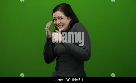 Frau, die Nervosität in grünem Hintergrund ausdrückt, ihre Emotionen in lebendigen Details erfasst und Angst und Unsicherheit zeigt. Stockfoto