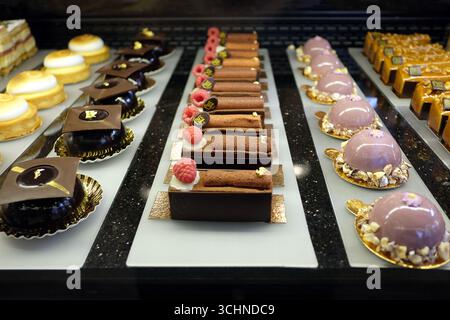 Es gibt verschiedene französische Backwaren und Kuchen, die ordentlich auf glänzend weißen Tabletts über einer schwarzen Granittheke angeordnet sind, eine köstliche Auswahl an Desserts Stockfoto