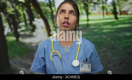 Junge hispanische Ärztin mit Stethoskop in einer Parkumgebung, trägt eine Uniform, vermittelt ein Outdoor-Gesundheitsthema mit Natur Hintergrund. Stockfoto