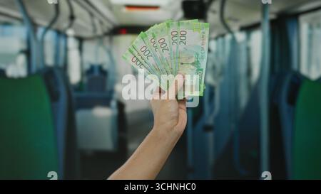 Hand eines kaukasiers, der russische Rubel-Banknoten in einem Bus hält und Geld in öffentlichen Verkehrsmitteln zeigt. Stockfoto