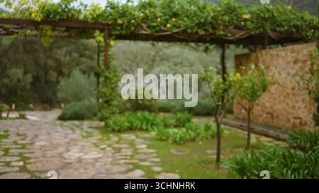 Verschwommene Gartenszene mit mediterranen Wegen und Grün mit defokussierten Steinmauern und üppiger Vegetation, die einen ruhigen Bokeh-Effekt schaffen Stockfoto