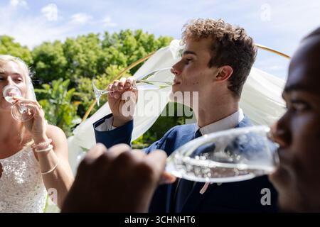 Gäste genießen Champagner im Freien während einer fröhlichen Hochzeitsfeier unter sonnigem Himmel Stockfoto