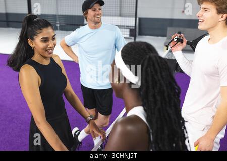 Verschiedene Tennisteams, die sich auf dem purpurroten Platz mit Schlägern und Fitness-Tracker unterhalten Stockfoto