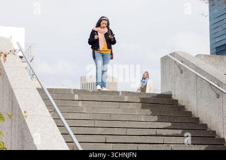 Reife Erwachsene Frau mit Smartphone, ältere afroamerikanerin, die die Treppe auf der plaza hinabsteigt Stockfoto