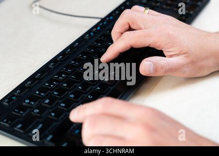 Draufsicht der Finger, die schwarze Tasten auf der Computertastatur, am Arbeitsplatz und im technologischen Kontext drücken Stockfoto