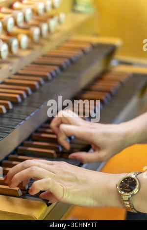 Eine Musikerin spielt ein Stück auf einer antiken Holzorgel in einer ruhigen lutherischen Kirche, ihre Hände bewegen sich anmutig über die Tasten. Stockfoto