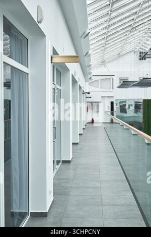 Moderner leerer Flur mit Glasgeländern und großen Fenstern, die zeitgenössisches architektonisches Design widerspiegeln, heller Innenraum mit hohen Decken und Oberlichtern, keine Personen sichtbar Stockfoto