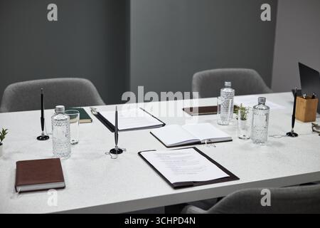 Leerer Konferenztisch mit offenen Notizbüchern, gedruckten Dokumenten, Glasflaschen, Stiften und kleinen Topfpflanzen für anstehende Geschäftstreffen Stockfoto