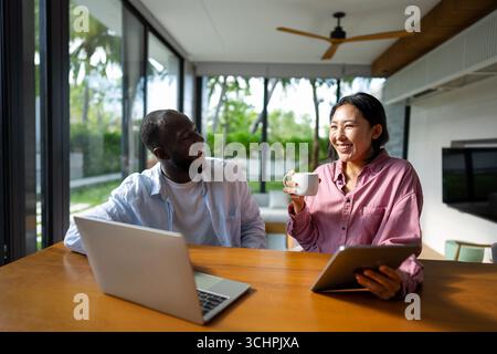 Geschäftsteam, zwei glückliche, vielseitige, multiethnische Führungskräfte, die im Büro mithilfe eines Laptops zusammenarbeiten. Stockfoto