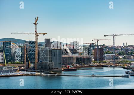 Baustelle mit Kranen am Oslofjord Oslo Norwegen // OSLO, Norwegen — Baukräne sind an einem Entwicklungsstandort am Oslofjord in Oslo, Norwegen, aktiv. Die städtische Landschaft bietet eine Mischung aus moderner Architektur und älteren Gebäuden, mit einem klaren blauen Himmel über dem Himmel. In diesem Gebiet wird eine erhebliche Stadterneuerung und -Expansion durchgeführt. Stockfoto