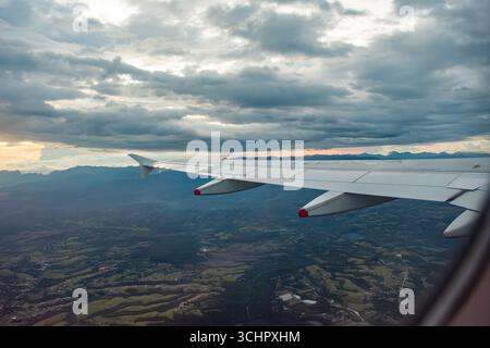 Atemberaubende Aussicht aus der Luft von einem Flugzeugflügel über üppige Landschaften und dramatische Wolken, die die Schönheit der kolumbianischen Landschaft einfangen. Stockfoto