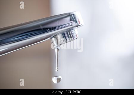 Tropfender Wasserhahn mit Wassertropfen im Badezimmer des Apartments. Makro, Nahaufnahme, geringe Schärfentiefe, keine Personen Stockfoto