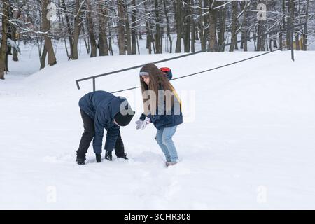 Zwei Kinder, ein Junge und ein Mädchen, werden beim Spielen im Schnee gesehen, scheinbar beim Bau einer kleinen Schneefestung oder eines Haufens. Sie sind gebündelt in warmer Winterkleidung Stockfoto