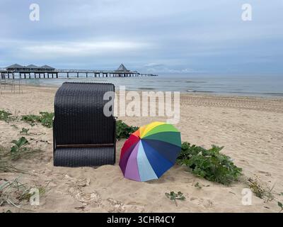Ein Regenbogenschirm in Stolz liegt am Sandstrand in der Nähe einer Liege am Pier von Heringsdorf, Usedom. Deutschland. Foto: Willy Matheisl Stockfoto
