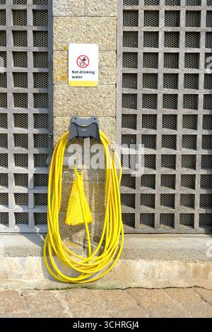 Cornwall, England, Großbritannien – Ein leuchtend gelbes Schlauchrohr, das an einem Wasserhahn aufgerollt ist und an einem öffentlichen Ort verwendet werden kann. Stockfoto