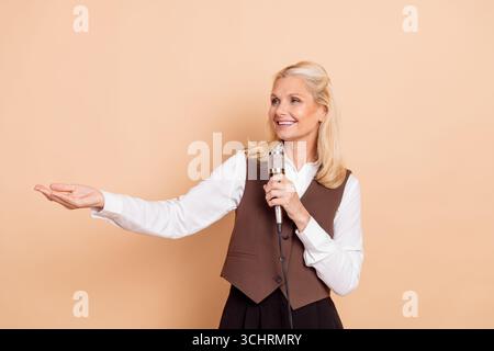 Professionelle Geschäftsfrau mit Mikrofon und Gesten auf beigefarbenem Hintergrund, zeigt Eleganz und Professionalität Stockfoto