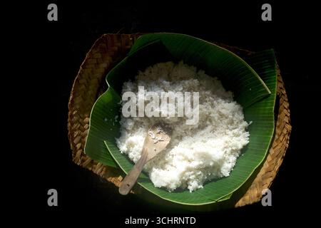 Gekochter weißer Reis, serviert auf grünen Bananenblättern mit einem Holzlöffel. Stockfoto