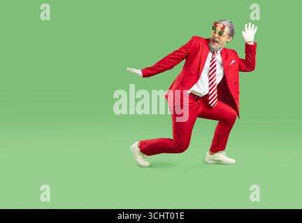 Der junge Weihnachtsmann in einem stilvollen roten Anzug und einer gestreiften Krawatte tanzt herum. Stockfoto