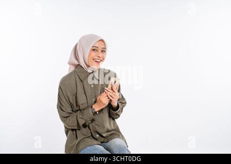 Eine fröhliche junge Frau hält ein Smartphone in einer ansprechenden Studio-Umgebung Stockfoto