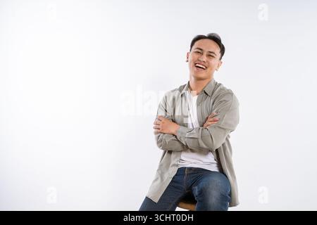 Ein glücklicher junger Mann, der auf einem Hocker-Studio-Porträt voller Leben und Freude sitzt Stockfoto