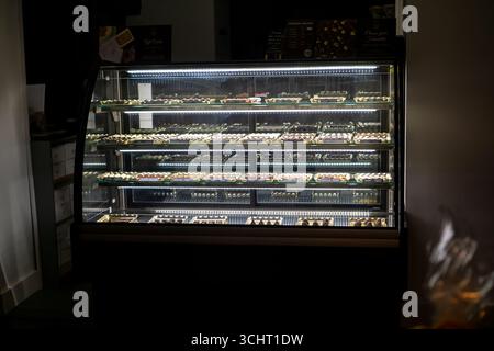 Eine gekühlte Vitrine voller Schokolade wird nachts hell beleuchtet und zeigt eine Auswahl an Konfekt bei Nacht in Saffron Walden. Stockfoto