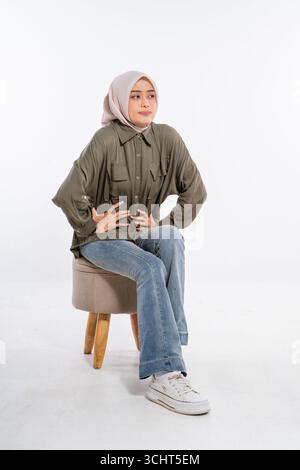 Eine junge Frau in lässigem Outfit sitzt auf einem Hocker und posiert für stilvolle Fotos Stockfoto