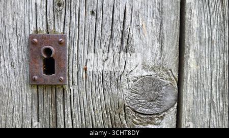 Nahaufnahme eines alten, rostigen Schlüssellochs in einer alten grau-schwarzen Holztür. Ein detailreiches rustikales Foto mit Texturen und Vintage-Charme Stockfoto