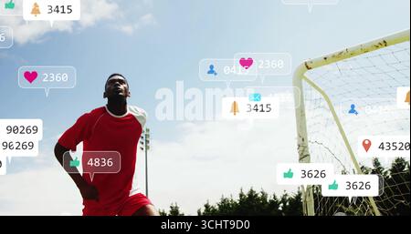 Stehender Fußballspieler in roter Uniform, der den Himmel neben dem Tor scannt, mit Social-Media-Symbolen im Kopierbereich Stockfoto