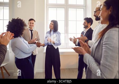 Glückliche, lächelnde Mitarbeiter begrüßen neue Mitarbeiter herzlich am Arbeitsplatz, freundliche Teamkollegen Stockfoto