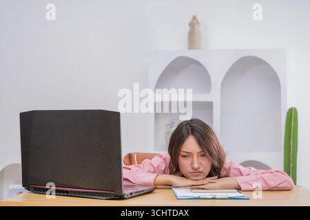 Frustrierte junge Frau, die von zu Hause aus mit einem Laptop auf dem Schreibtisch arbeiten muss Stockfoto